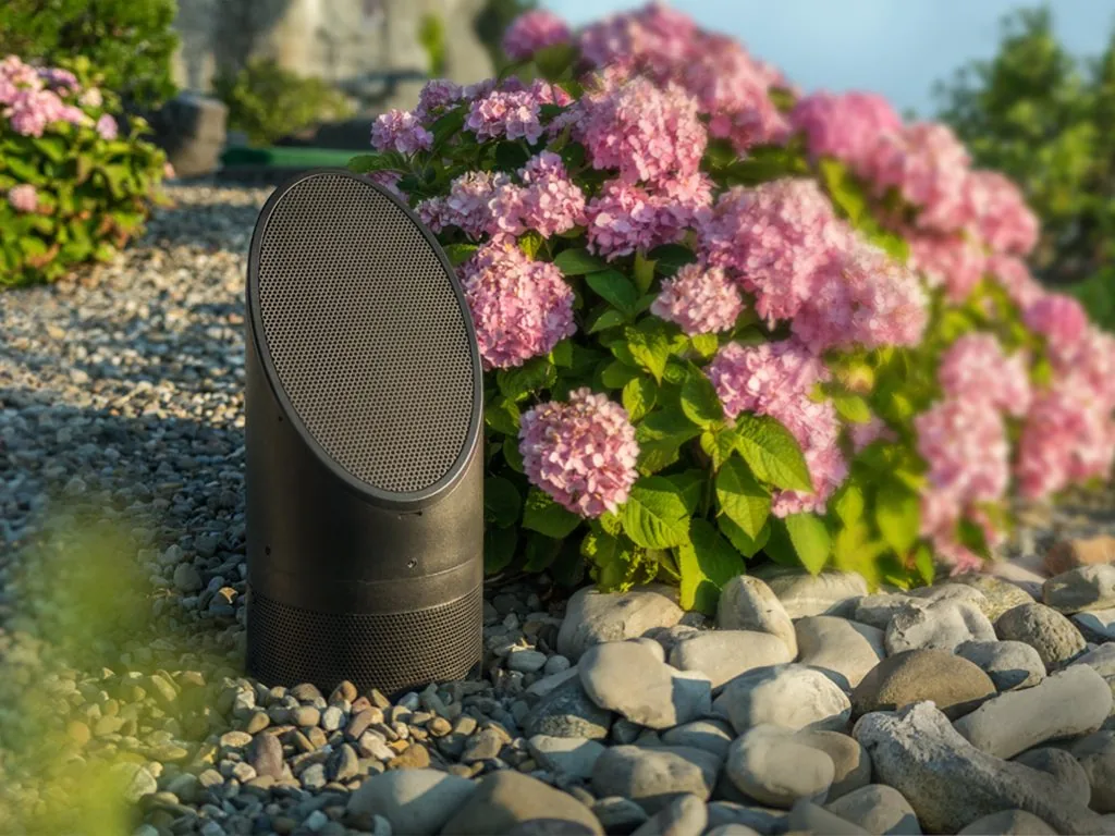A Coastal Source bollard speaker in gravel beside pink hydrangeas