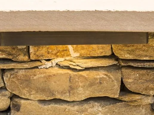A Coastal Source hardscape light under a stone wall cap, grazing the stone below