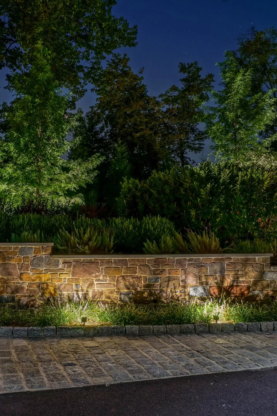 A stone garden wall washed with warm light at dusk, with trees uplit behind