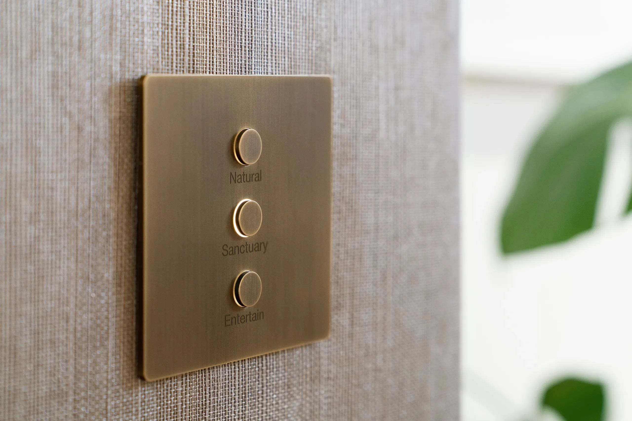 A Lutron Alisse keypad in brushed brass on woven wallpaper, engraved Natural, Sanctuary and Entertain