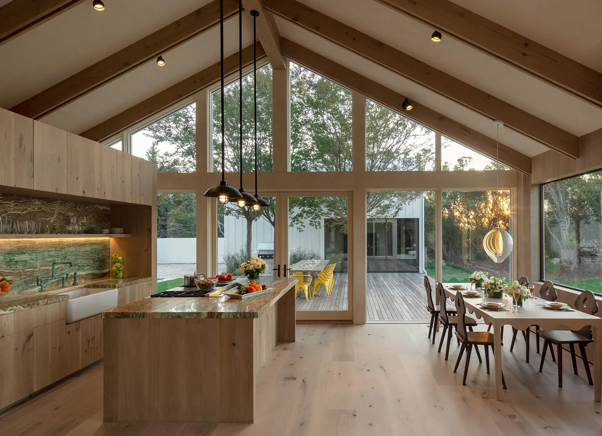 A kitchen and dining room under a vaulted ceiling, pendants lit as the light outside fades