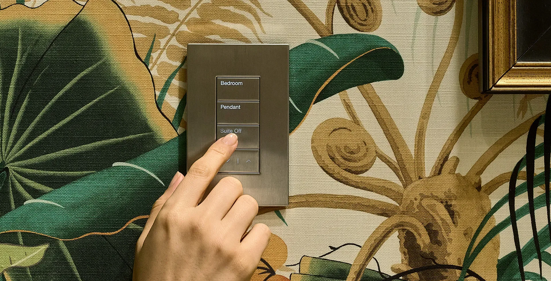 A hand on a Lutron Palladiom keypad set into patterned wallpaper, engraved Bedroom, Pendant and Lights Off