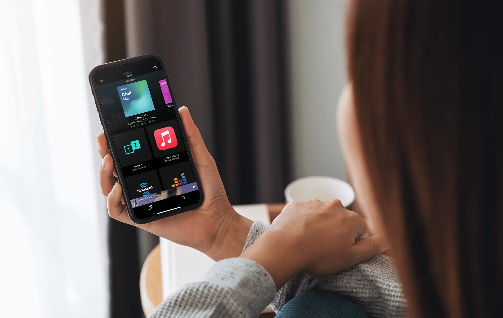 A phone showing the Savant app's music screen, held over a kitchen counter