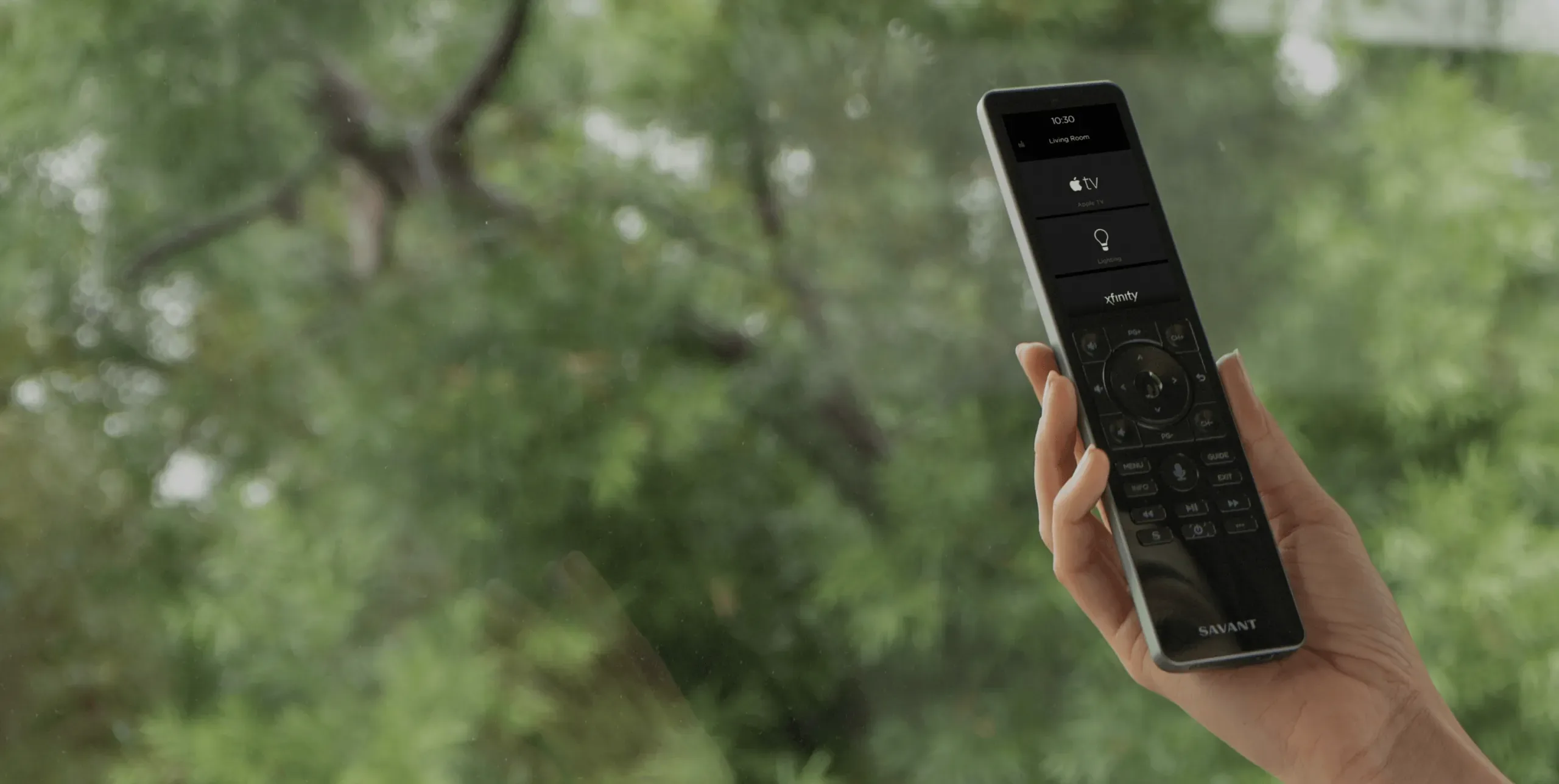 A hand holding a Savant Pro Remote in front of a garden