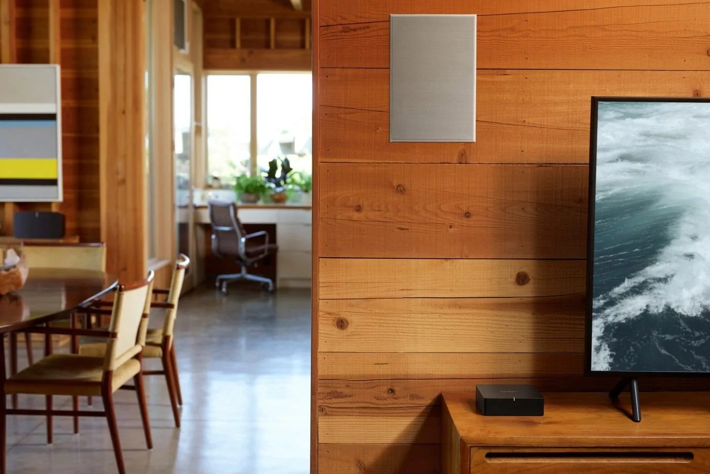A Sonos Port on a wooden sideboard with an in-wall speaker above and a television beside it